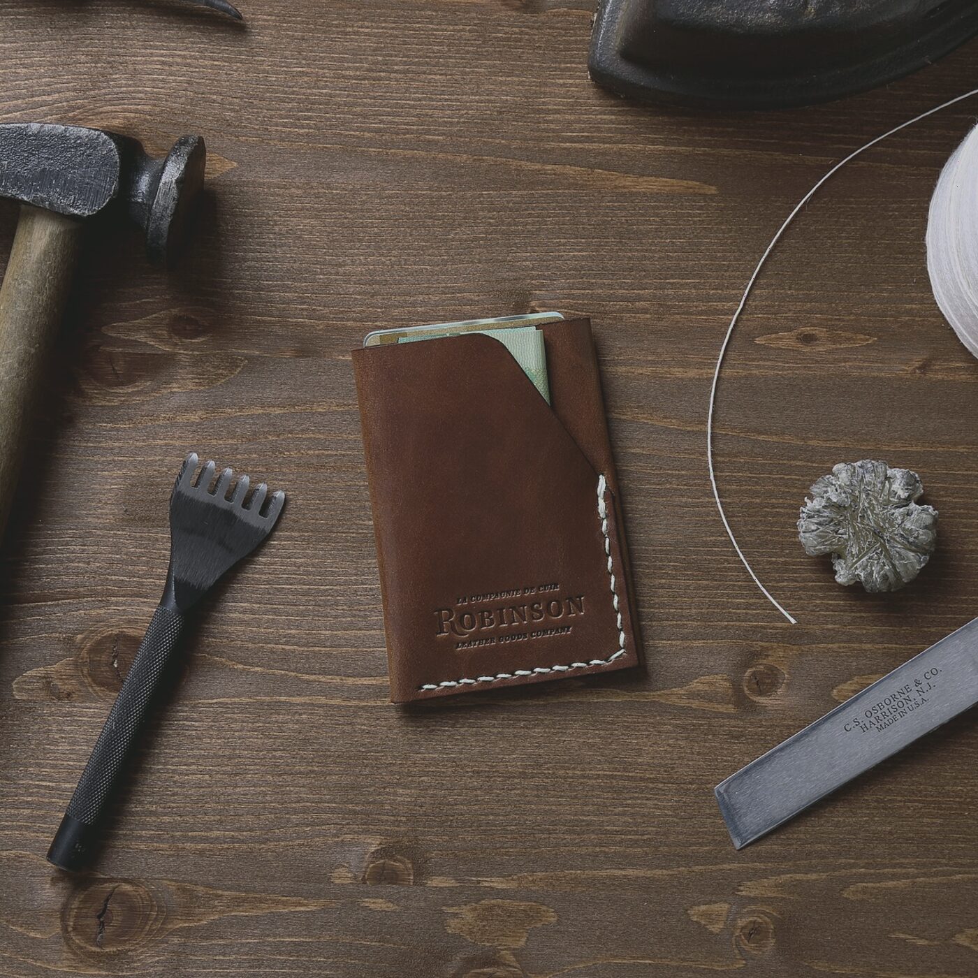 Hand-stitched leather pouch on a workbench with a needle and waxed thread