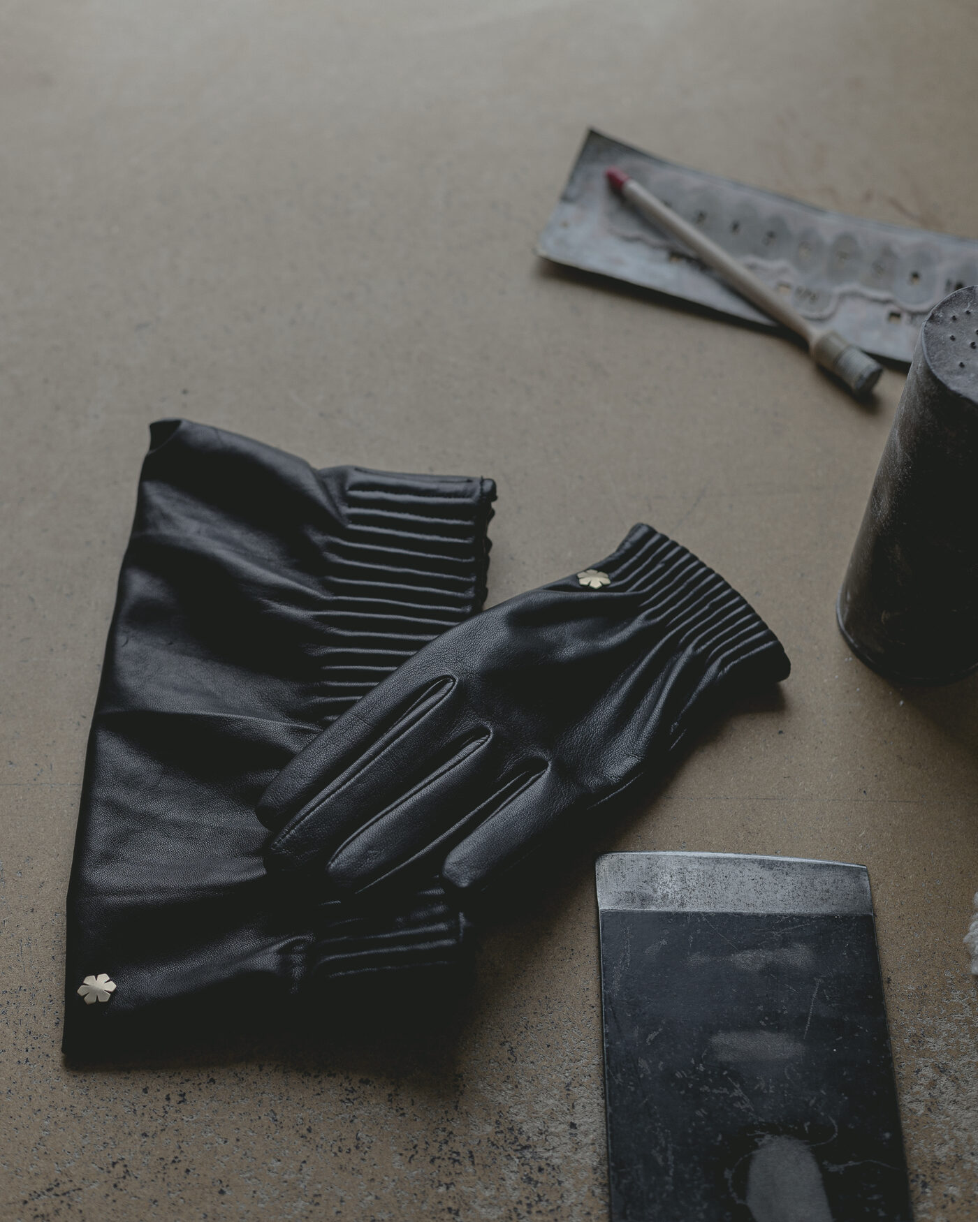 Black leather gloves resting beside tanning and finishing compounds on a bench