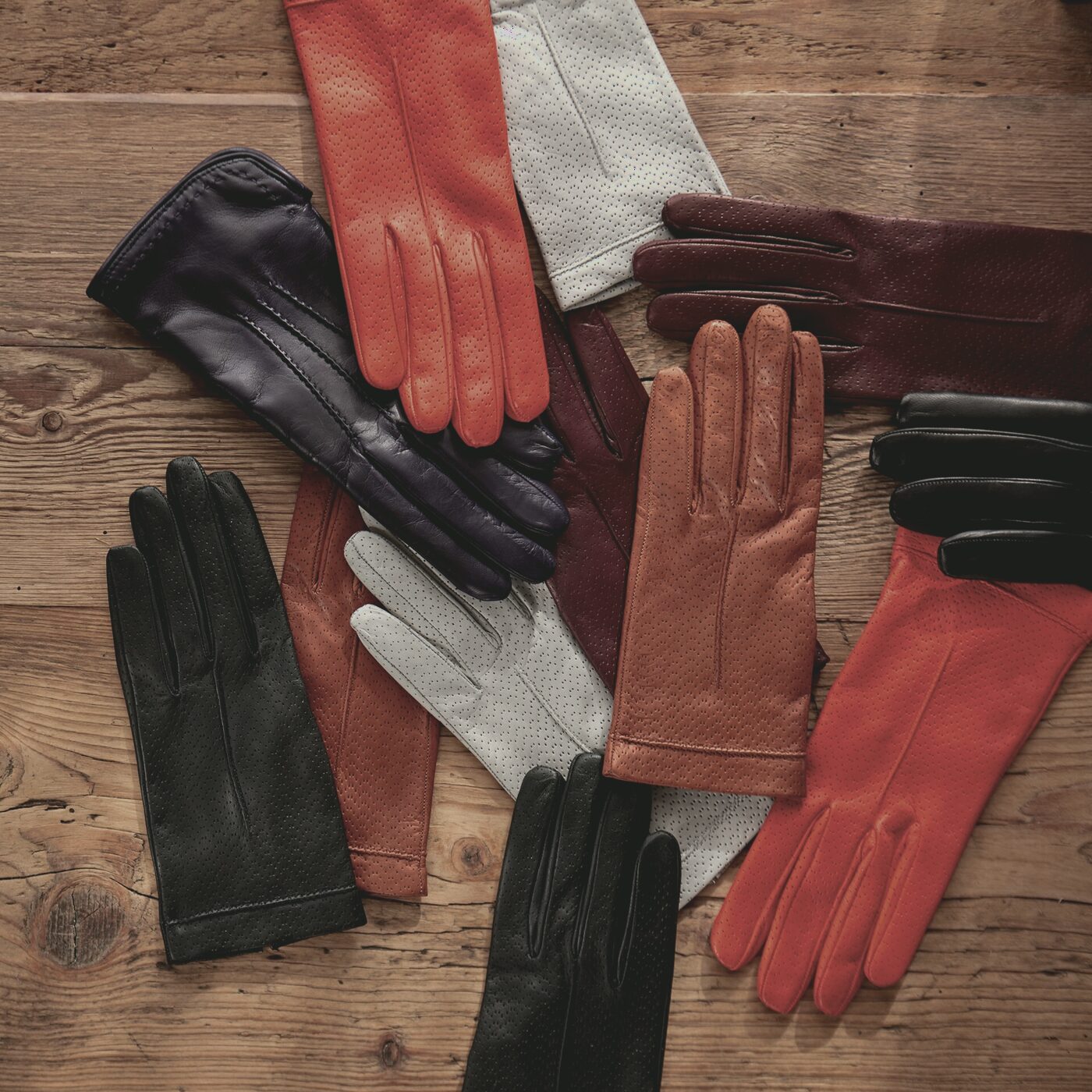 Finished leather gloves in a range of tones arranged by hand on a wooden bench