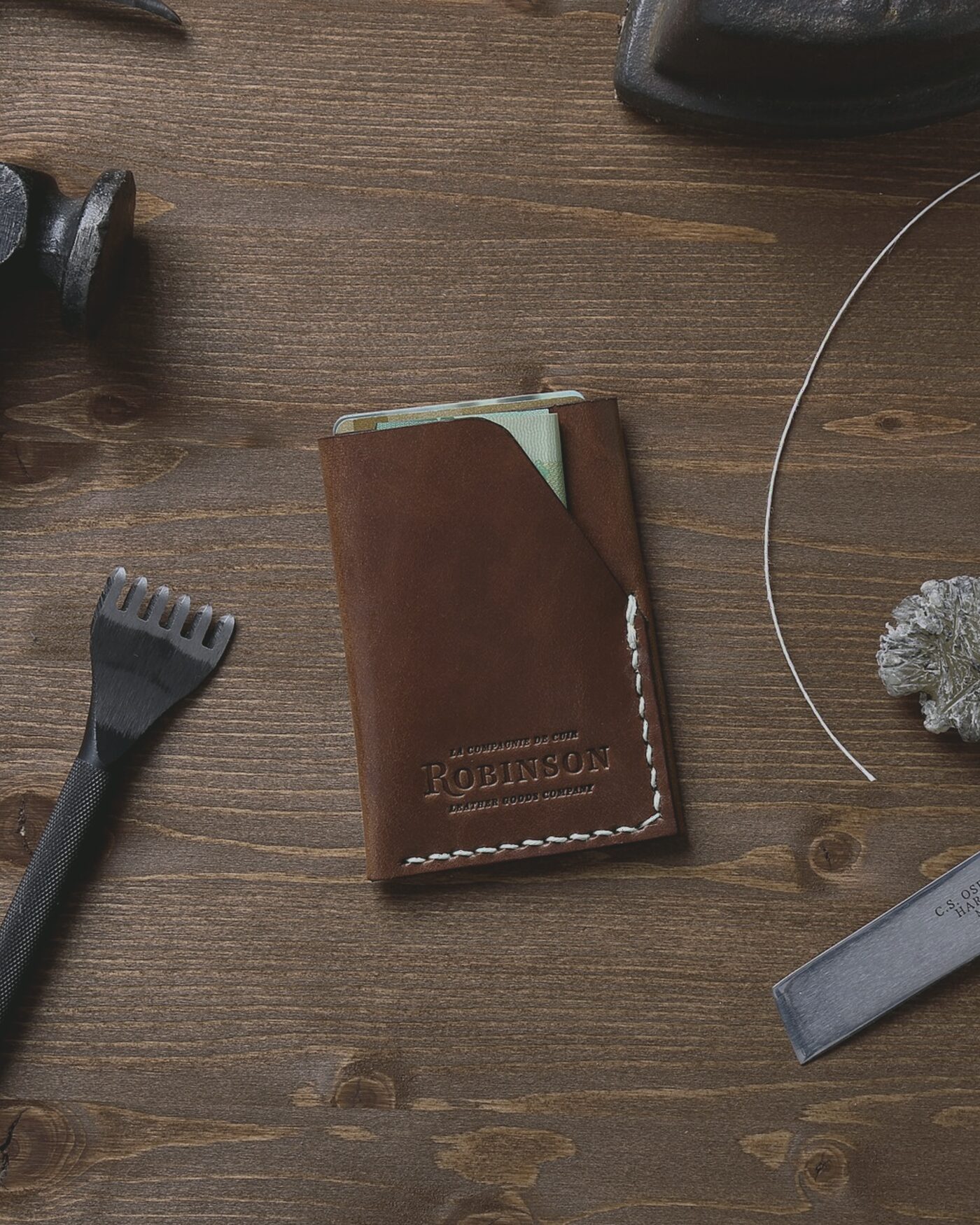 Hand-stitched leather pouch on a workbench beside a needle and waxed thread